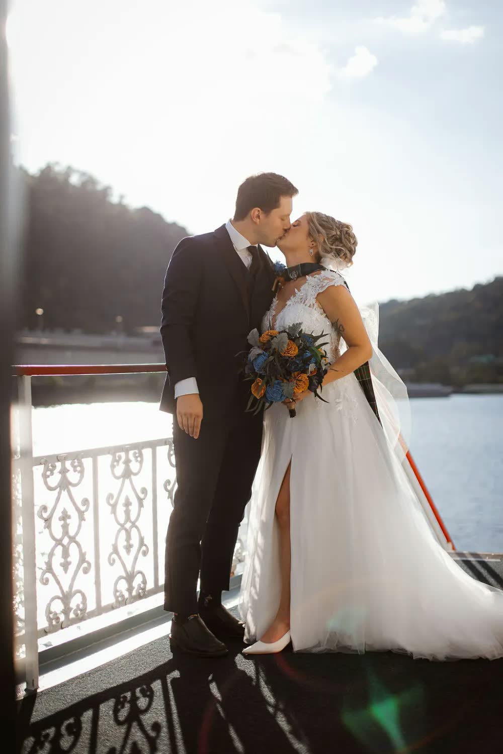 The newlyweds kiss at the ornate white rail of the riverboat in late-afternoon sunlight