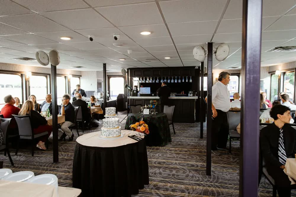 Guests mingling in the riverboat's dining room around a cake table, with the bar behind