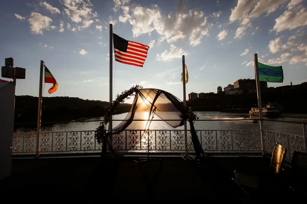 The sun setting behind the ceremony arch and flags on the riverboat's top deck