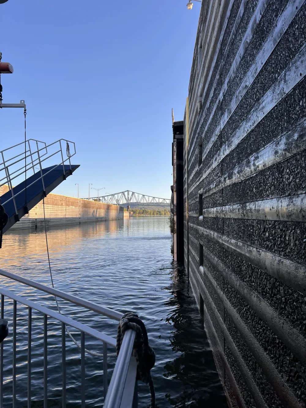 The Queen's railing and boarding ramp beside the tall concrete wall of a river lock, with a truss bridge in the distance