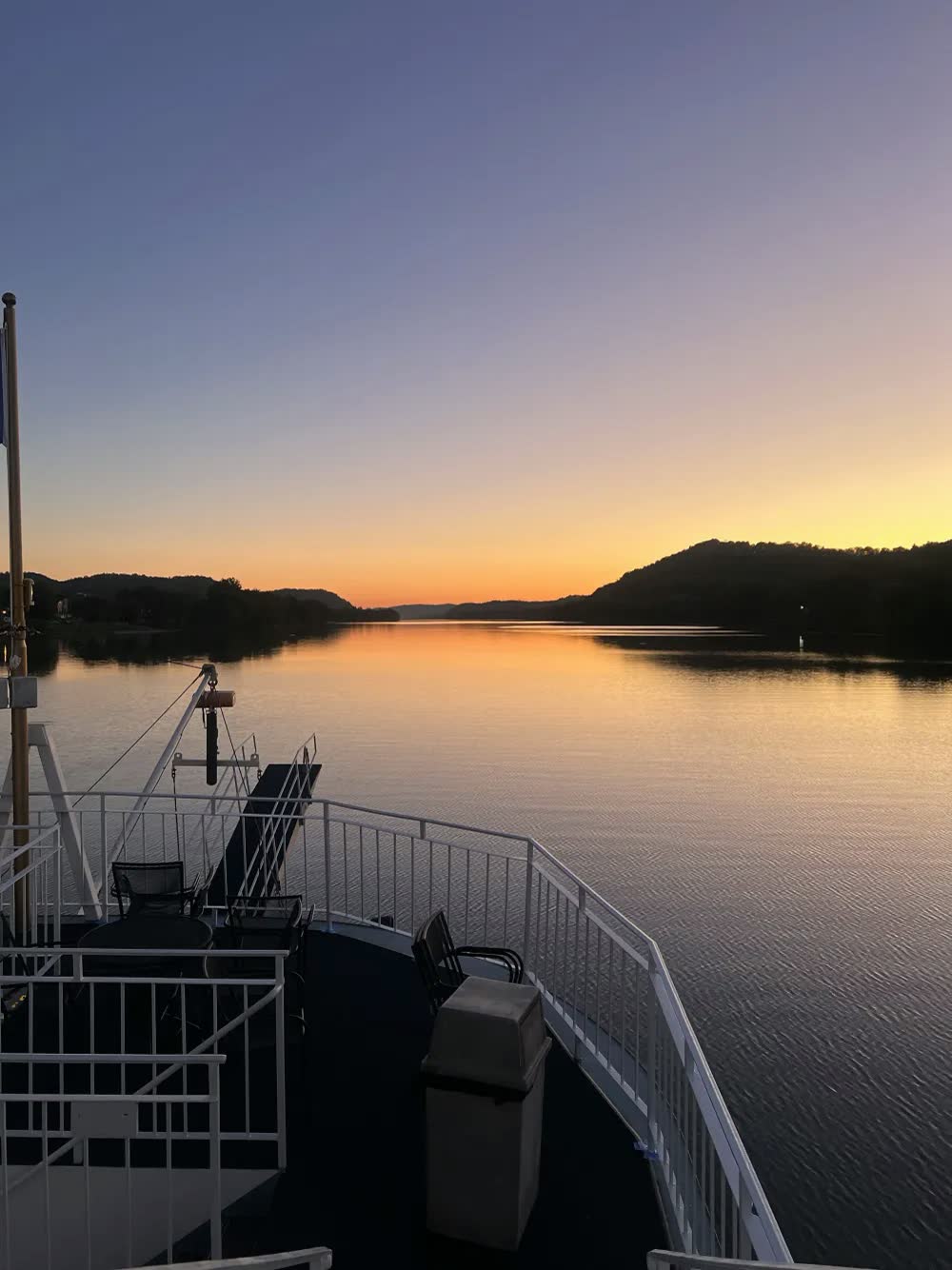 A golden sunset over the calm Ohio River and dark hills, seen from the Queen's bow