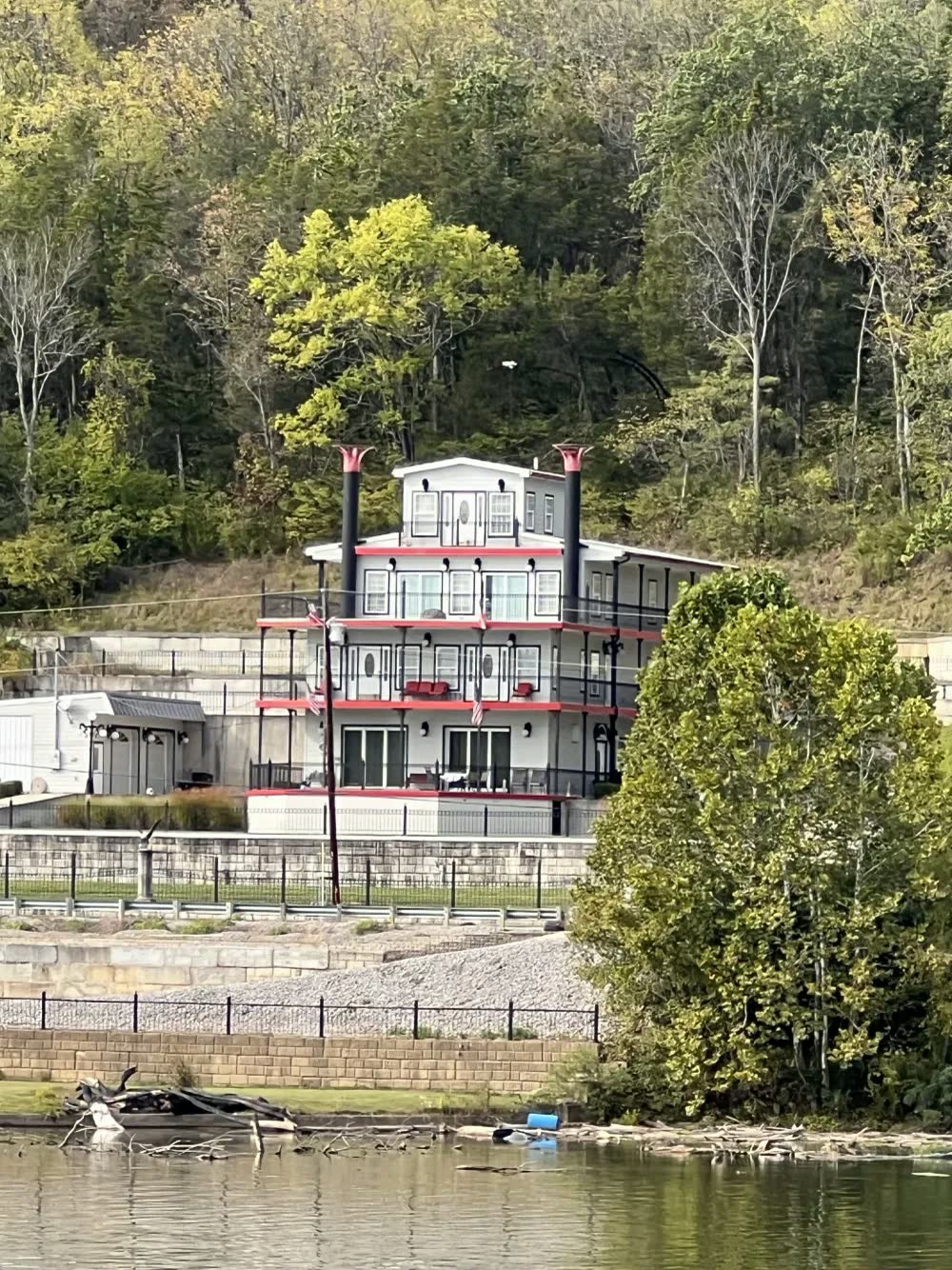 A white, red-trimmed house built to look like a riverboat with twin smokestacks, on a wooded hillside above the Ohio River