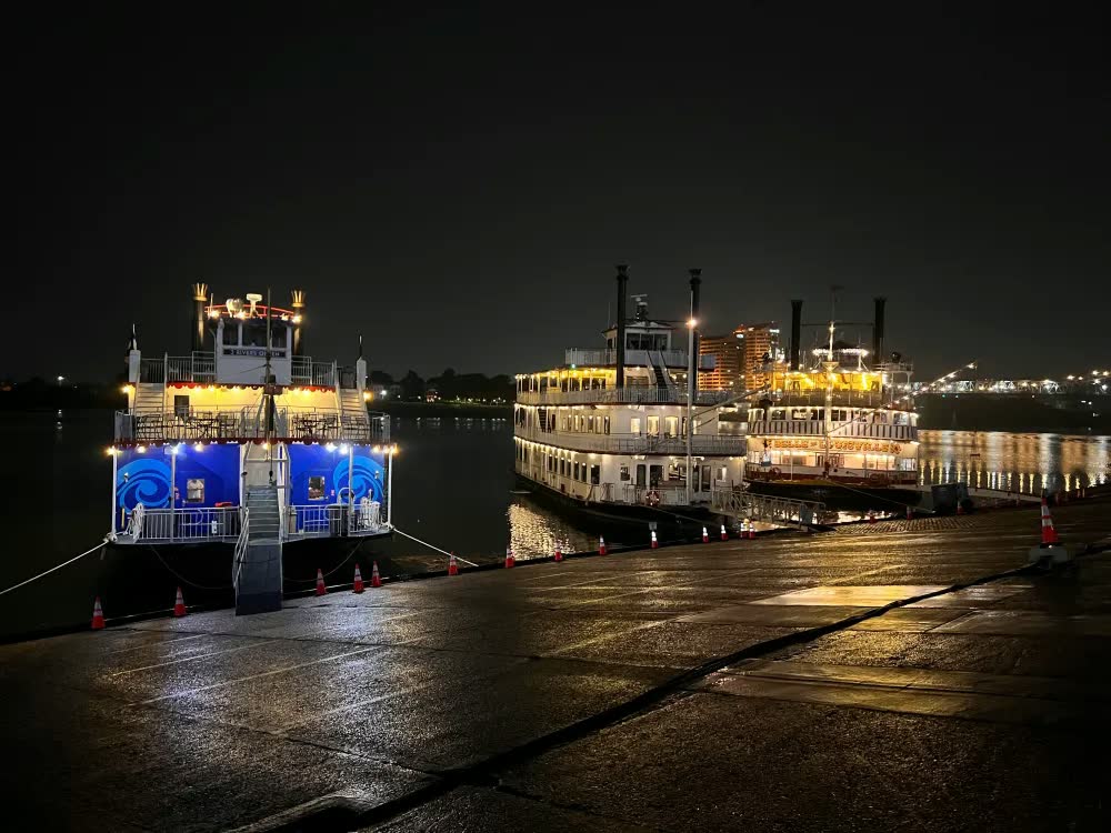 The Three Rivers Queen lit up at night at Cincinnati's public landing, docked near other paddlewheel riverboats