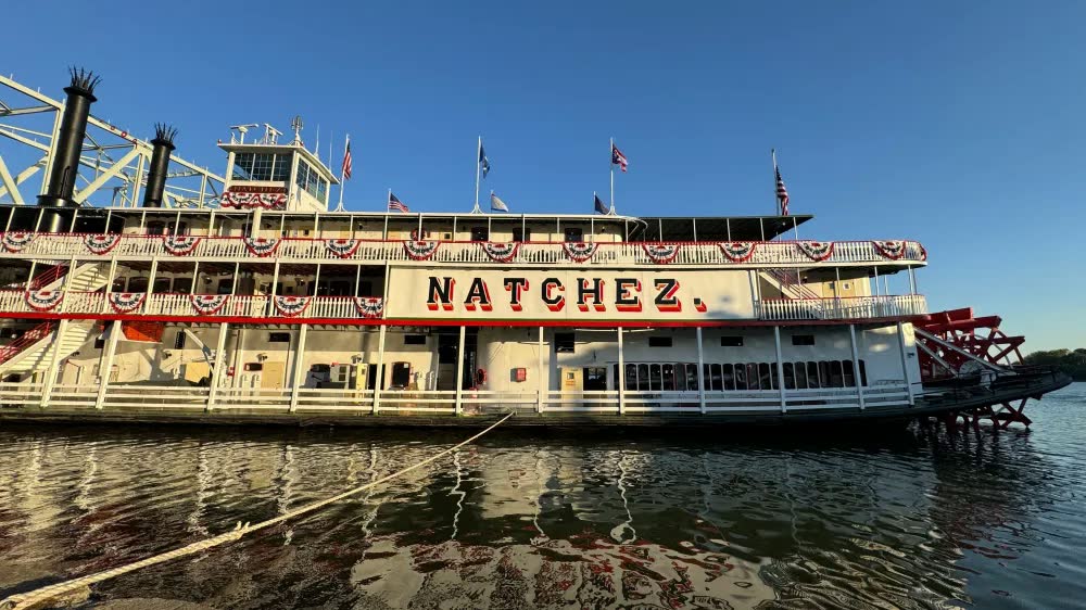 The Steamboat Natchez with red-white-and-blue bunting and its red paddlewheel, docked on the Ohio River