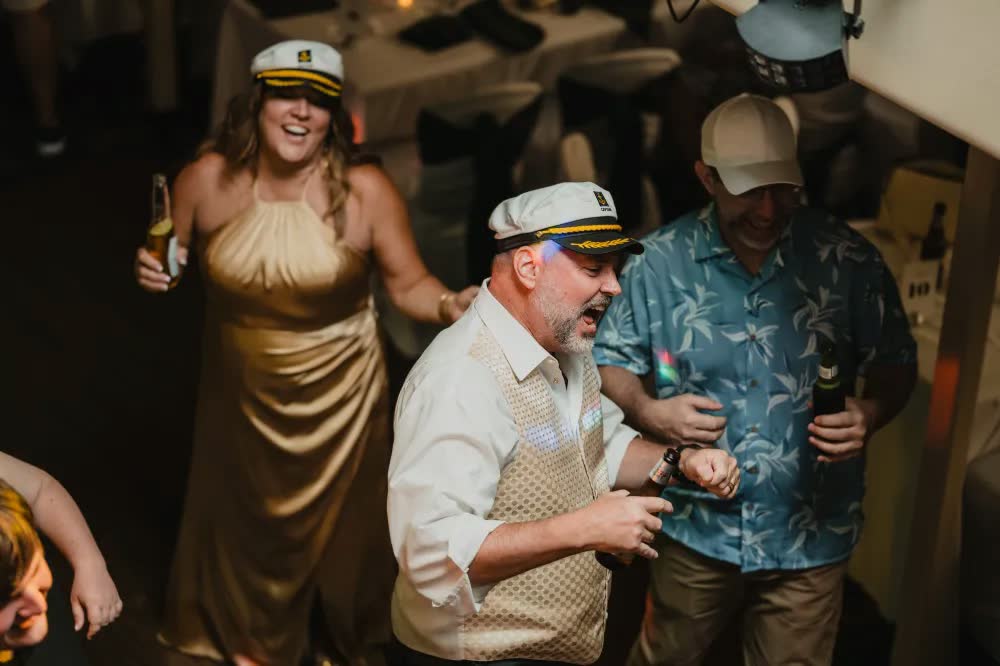 Wedding guests in captain's hats laughing and dancing at a yacht rock themed reception aboard a Gateway Clipper riverboat