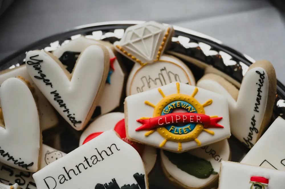 Custom wedding cookies with a Gateway Clipper Fleet ship's wheel logo, a diamond ring and a 'Dahntahn' skyline