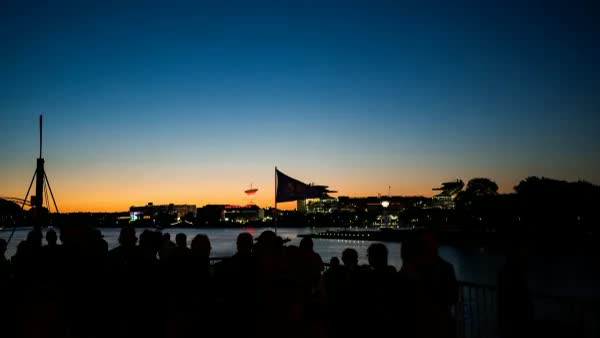 Guests silhouetted on a riverboat deck at dusk, with city lights across the water