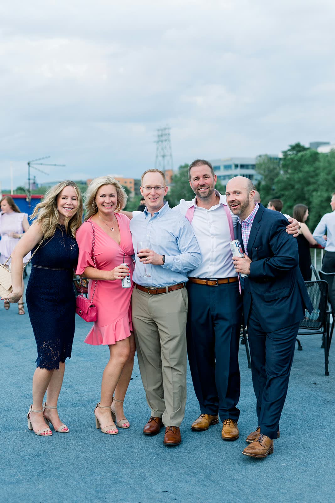 Guests posing together on the open top deck of a Gateway Clipper riverboat on a cloudy evening, with trees and buildings along the riverbank behind them