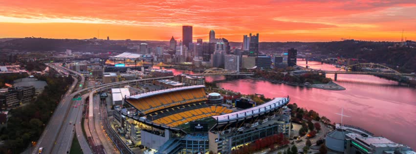 Pittsburgh skyline and Acrisure Stadium at sunset, with the rivers glowing pink and orange