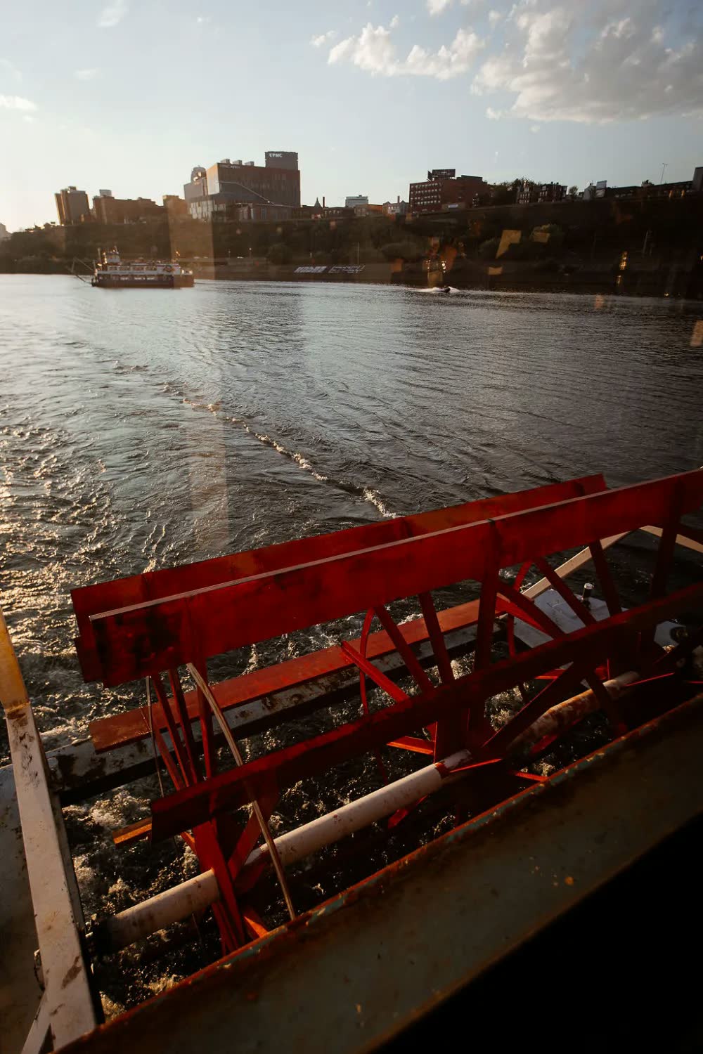 The red paddlewheel of a Gateway Clipper riverboat churning the river at sunset, with the city behind