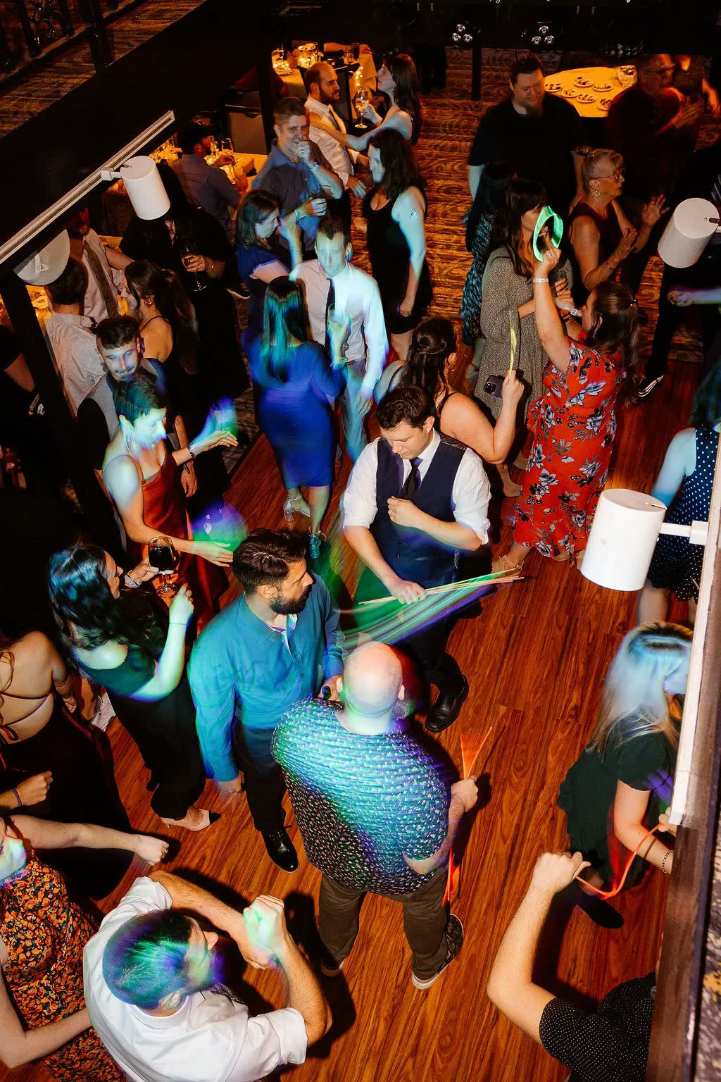 Guests in dressy outfits dancing with glow sticks on a riverboat dance floor, seen from above