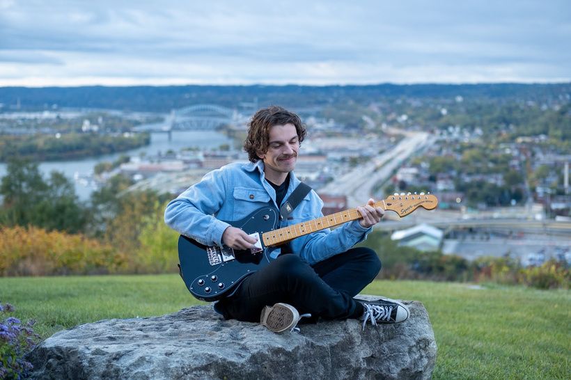 A musician playing guitar on an overlook above the Pittsburgh rivers