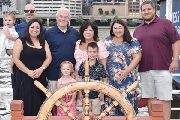 A family posing behind a wooden ship’s wheel on deck