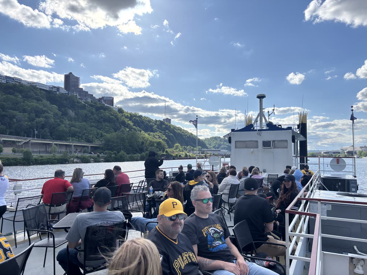 Fans in Pirates caps and jerseys relaxing on the open top deck of a Gateway Clipper riverboat on a sunny day