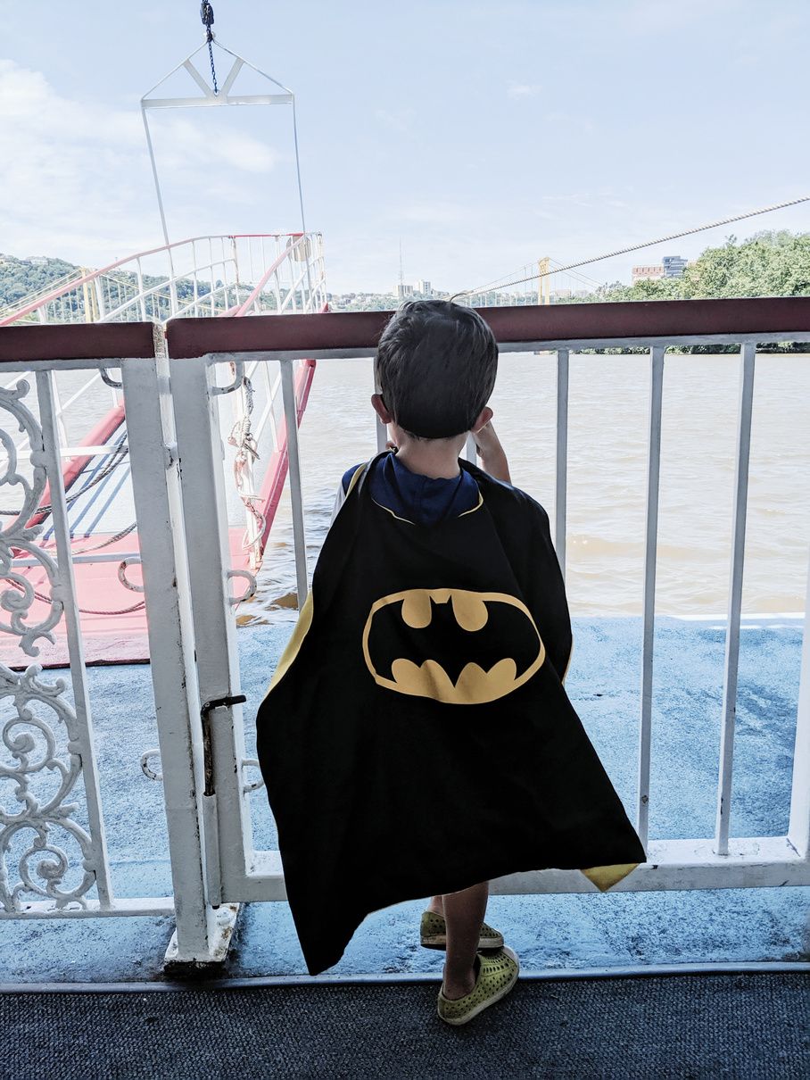 A child in a Batman cape looking out over the river from the rail
