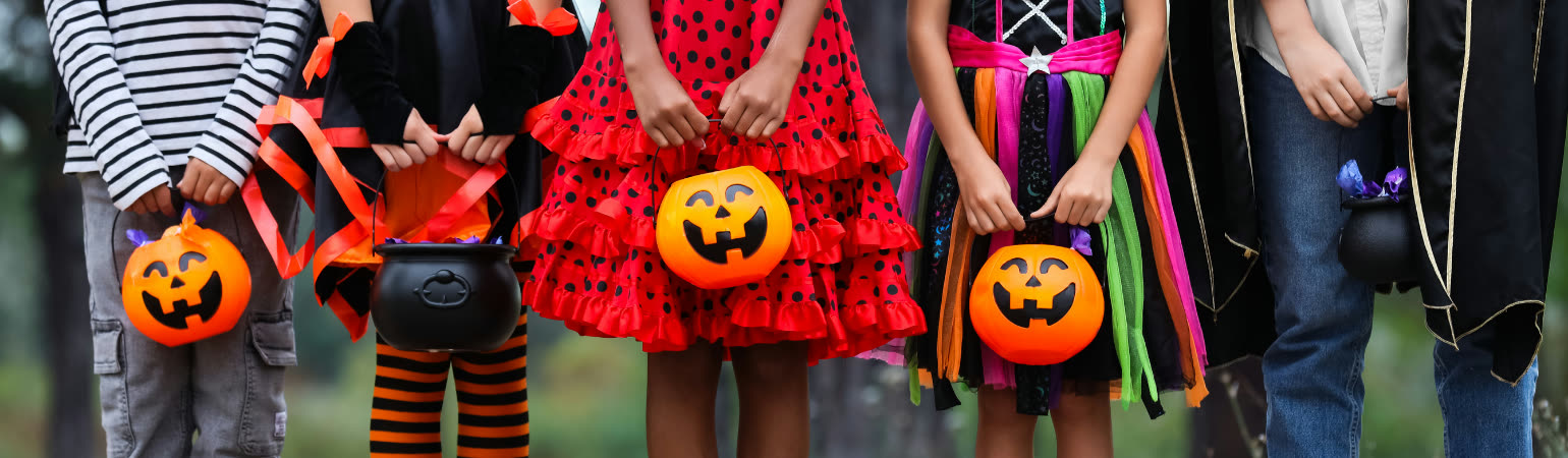 Children in Halloween costumes holding jack-o'-lantern candy buckets and a black cauldron