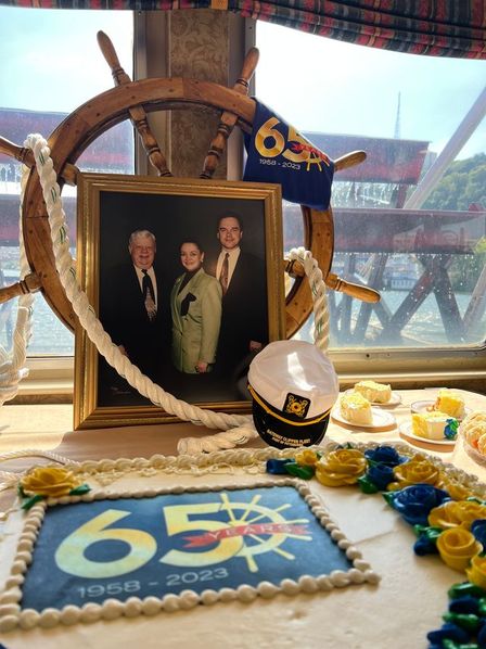 A 65th anniversary cake beside a ship's wheel, a captain's hat and a framed family photo