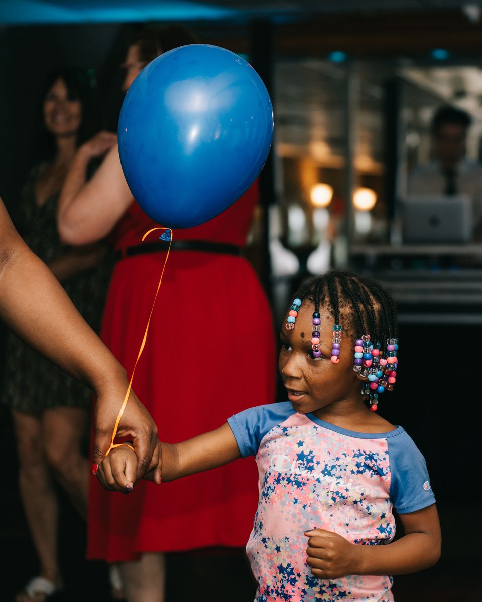 A little girl with beaded braids holding a grown-up's hand and a blue balloon on a riverboat dance floor