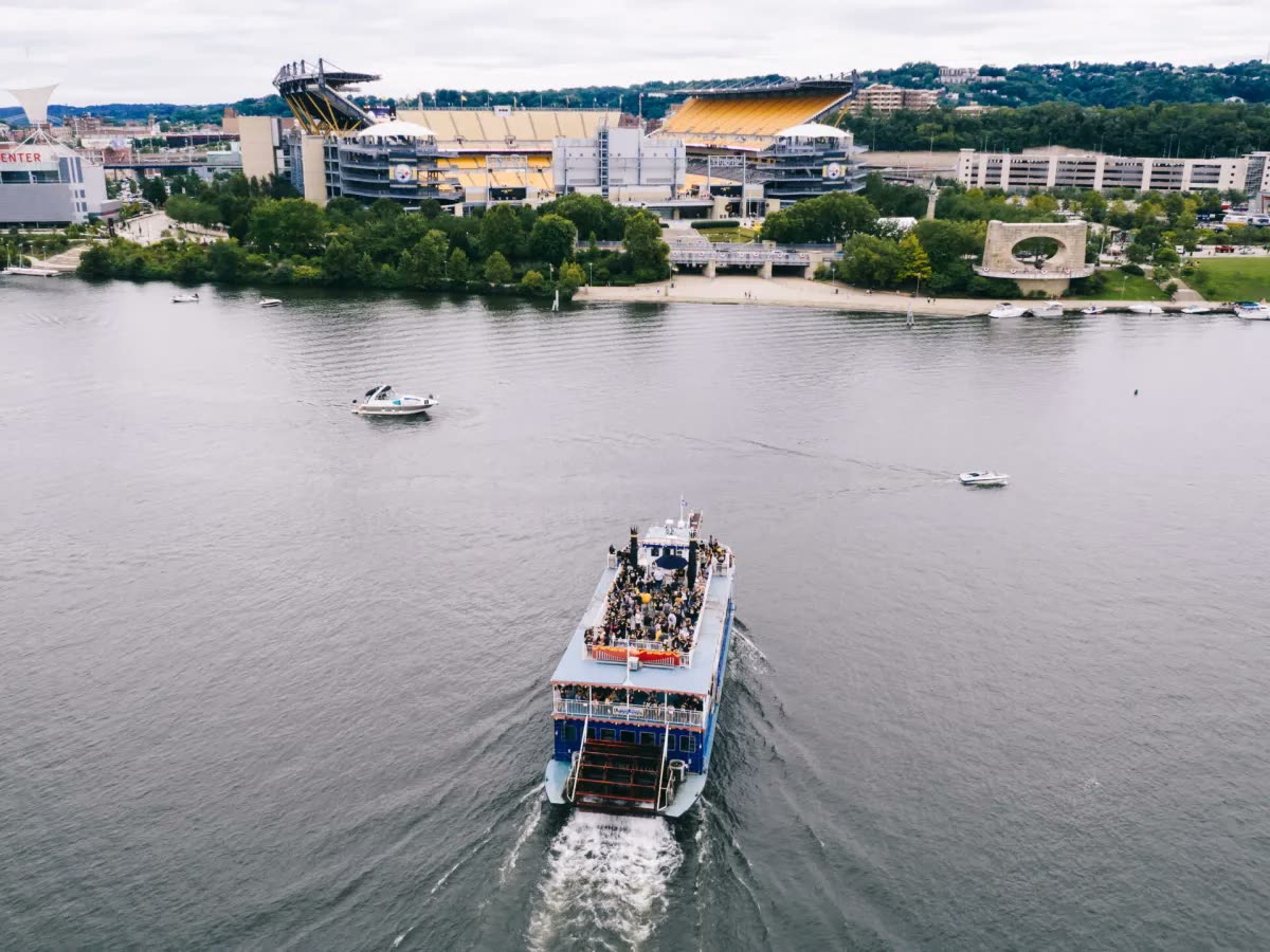 Aerial view of a Gateway Clipper riverboat full of fans crossing the river toward Acrisure Stadium on the North Shore