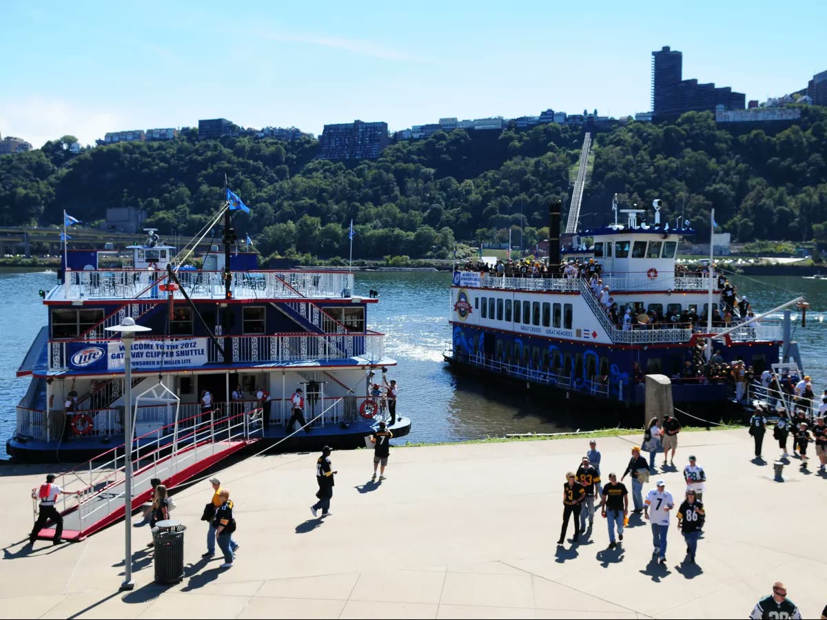 Steelers fans walking along the North Shore riverfront past two Gateway Clipper riverboats docked for game day
