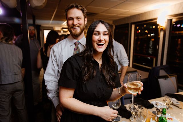 A couple smiling and holding a glass of wine aboard