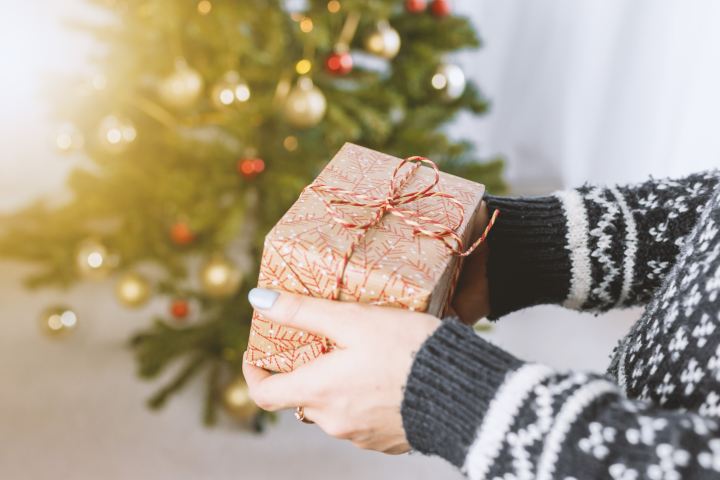 woman holding christmas present with christmas tree in background