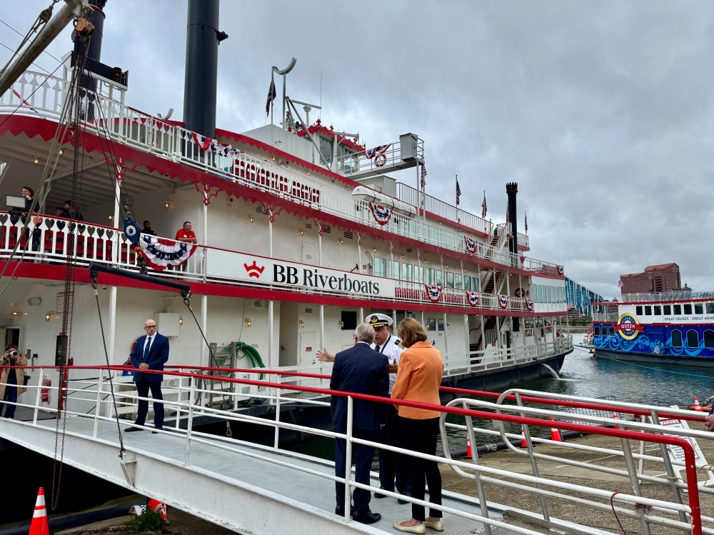A riverboat named 'BB Riverboats' docked, with people boarding and crew members present on a cloudy day.