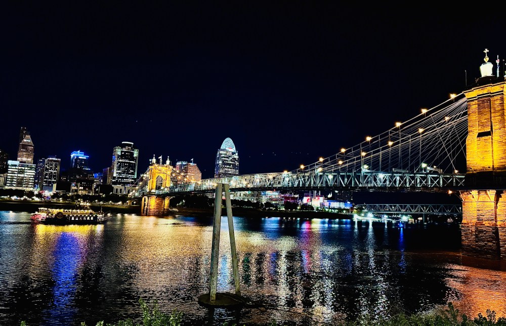 Night view of a suspension bridge and city skyline reflected in a river.