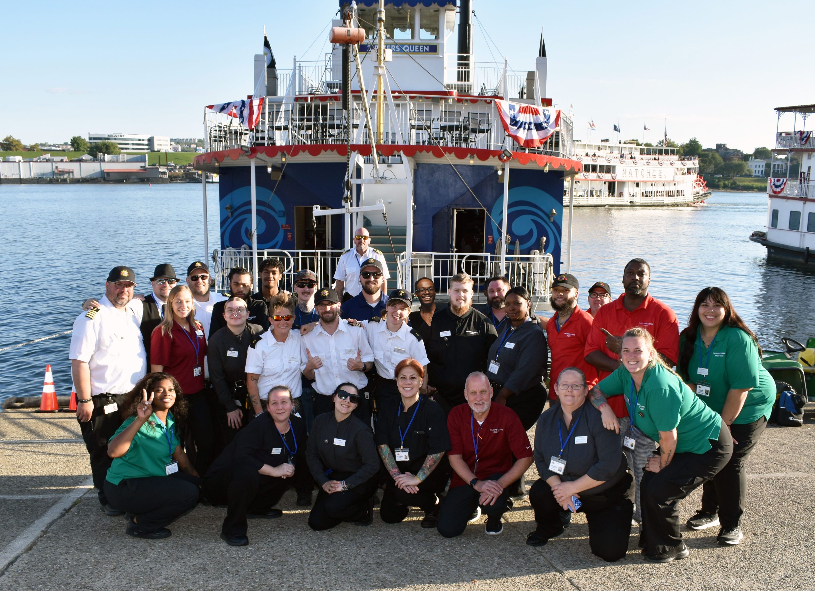 Group of people in uniform posing in front of a riverboat on a sunny day.